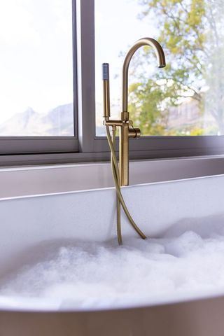 Brushed-gold freestanding bathtub faucet with hand sprayer window overlooking mountain view