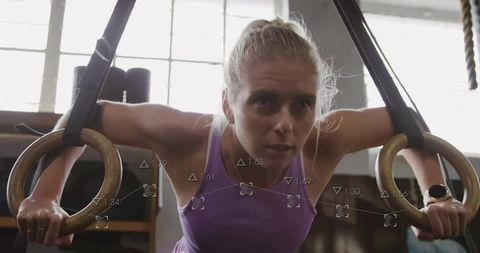 Determined woman performing suspension ring workout in gym