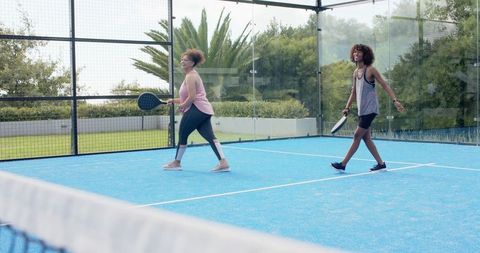 African american friends walking on blue padel court wearing athletic activewear