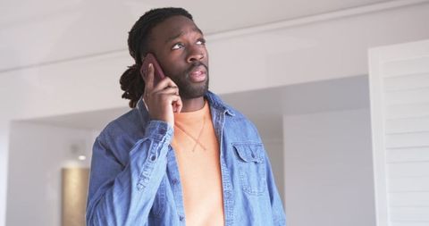 African american man talking on smartphone in modern apartment looking thoughtful