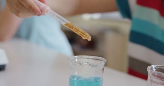 Midsection of caucasian schoolboy using pipette for experiment in elementary school science class. Chemistry, science, childhood, education, learning and elementary school, unaltered.