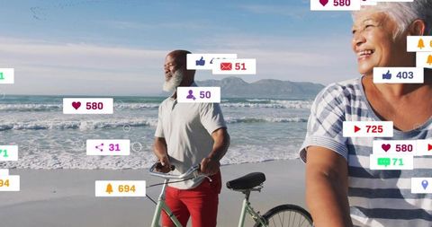 Mature couple walking with bicycles on sunny beach surrounded by digital social media icons