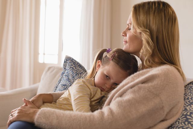 Mother holding and comforting her upset daughter on a couch at home. This image can be used for articles or advertisements related to parenting, family relationships, emotional support, and child care. It highlights themes of love, comfort, and the bond between a mother and her child.