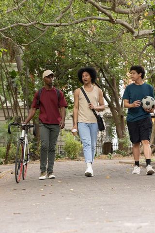 African american friends walking in park with bicycle, soccer ball, coffee enjoying stroll