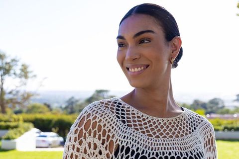 African american woman smiling outdoors wearing white crochet top and gold earring