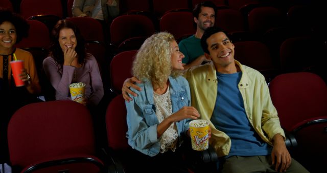 Group of friends of various ethnic backgrounds enjoying a movie together in a cinema. They are smiling, laughing, and having fun while sharing popcorn. Ideal for use in topics related to friendship, entertainment, leisure activities, and multicultural bonding experiences. Can be used for advertisements, social media posts, or websites promoting movie theaters or social activities.