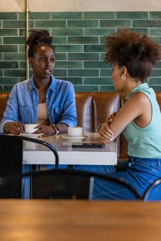 Two african american women chatting over coffee in cozy urban cafe with green subway tile