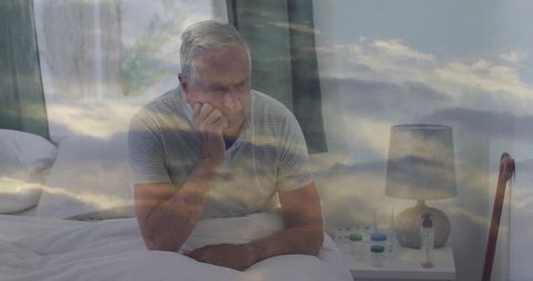 Senior man sitting on bed resting head and gazing, contemplative elder with pills and cane