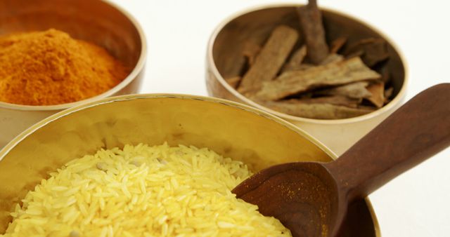Close-up view of assorted Indian spices including turmeric, rice, and dried bark. Highlights traditional Indian cooking ingredients in metallic bowls with a wooden spoon. Perfect for use in cooking blogs, culinary magazines, and food marketing materials.