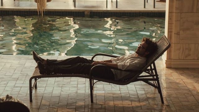 Man relaxing on woven lounge chair by sunlit pool with reflective water