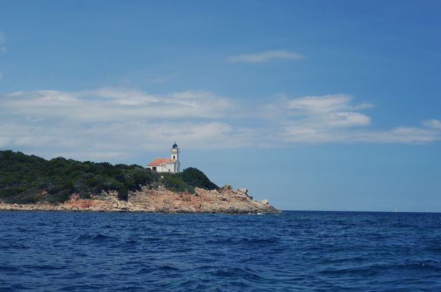 Beautiful scene featuring a lighthouse perched on a rocky coastline overlooking the calm ocean under a clear blue sky. Great for use in travel brochures, maritime publications, and nature websites. Ideal for concepts of navigation, serenity, and coastal landscape.