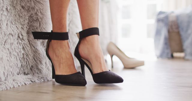 Close-up view of a woman's legs wearing black high heels in a stylish indoors setting. Ideal for use in fashion and footwear advertisements, social media promotions, fashion blogs, or online shops showcasing elegant women's shoes.