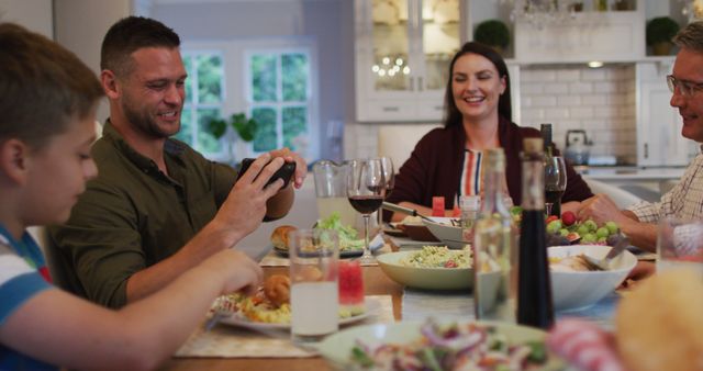 Family enjoying meal at home. Adult taking photo with smartphone while others smile and engage. Suitable for family, lifestyle, and togetherness themes in blogs, advertisements, and social media campaigns.