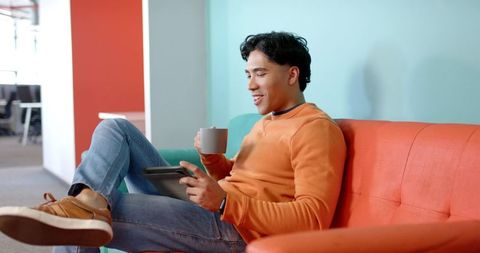 Young man relaxing on sofa in coworking lounge with tablet and coffee