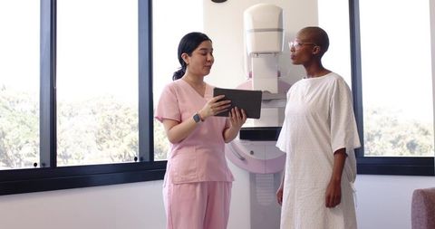 Nurse explaining mammography procedure to patient using tablet beside mammography unit