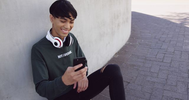 Young man outdoors smiling at phone with headphones around neck - Download Free Stock Images Pikwizard.com