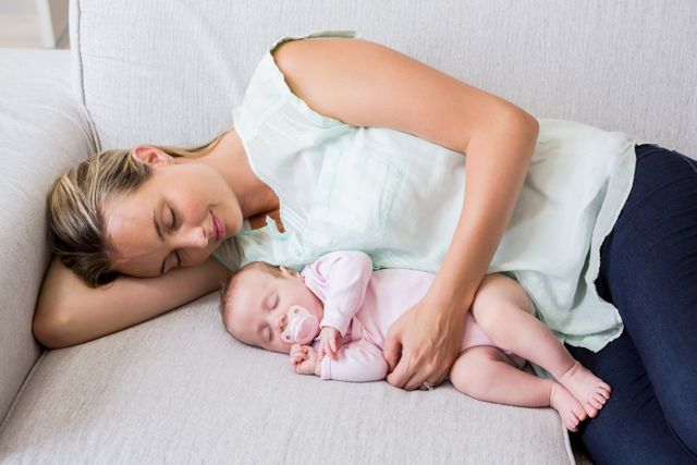 Mother and baby sleeping together on a couch, showcasing a tender moment of bonding and relaxation. Ideal for use in parenting blogs, family lifestyle articles, advertisements for baby products, and content related to motherhood and family life.