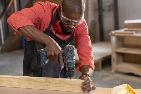 Carpenter drilling wooden plank using cordless drill workshop craftsmanship and safety
