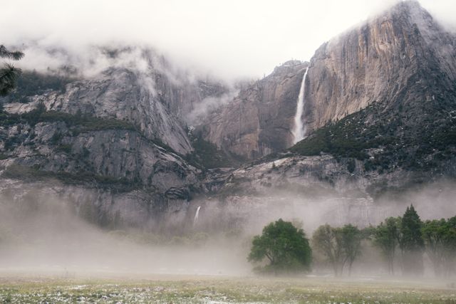 Captures picturesque scenery of Yosemite Valley with mist-shrouded mountains and cascading waterfall. Ideal for use in travel promotions, nature blogs, environmental awareness campaigns, and educational materials focused on natural parks and outdoor adventures.