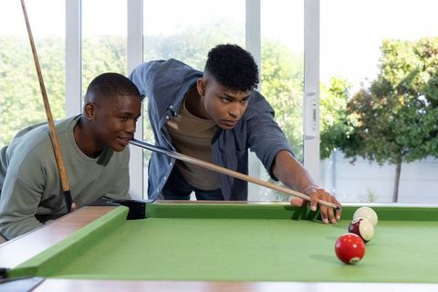 African american teens playing pool leaning over green felt table focusing on precision shot
