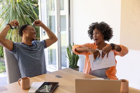 African american couple celebrating success at home office pointing to pie chart