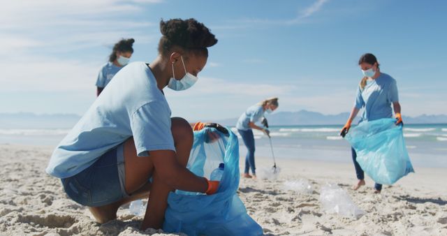 Diverse group of women wearing volunteer t shirts and face masks picking up rubbish from beach - Download Free Stock Photos Pikwizard.com
