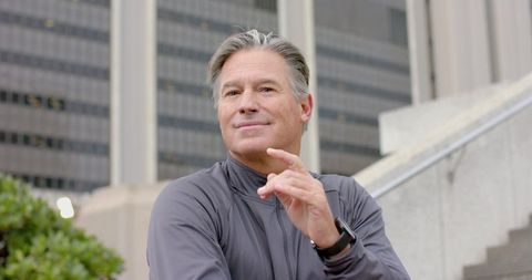 Mature man gesturing confidently on urban steps wearing smartwatch and zip-up jacket