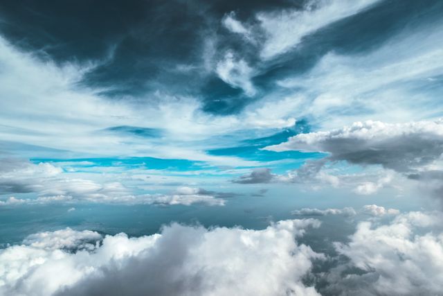 Photograph captures dramatic sky filled with various types of clouds at different elevations. Dense clouds appear in foreground, while patches of blue sky break through middle. Perfect for weather-related content, backgrounds, desktop wallpapers, nature-related articles, and social media posts highlighting natural beauty.