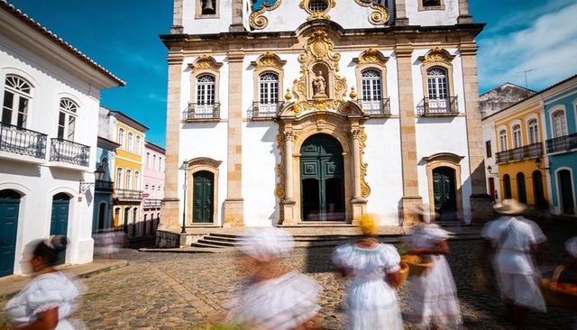 Baroque church facade with women parading on cobblestone in classic white dresses and headwraps