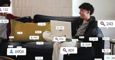 Smiling young man relaxing on sofa with laptop amid social media notification bubbles