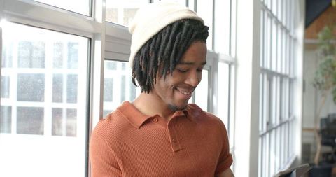 African american man leaning by window checking tablet in bright coworking workspace