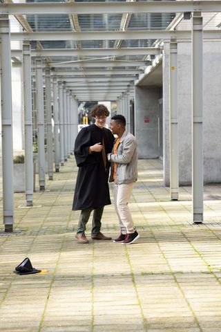 Graduation friends celebrating on campus walkway wearing academic gown with mortarboard