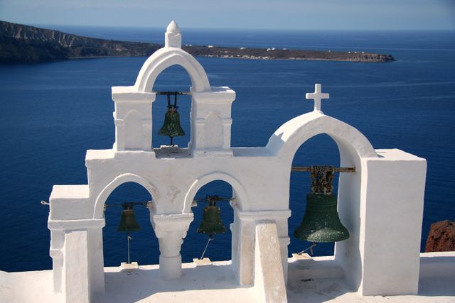 This peaceful scene showcases the iconic white bell tower of a church overlooking the blue Aegean Sea in Oia, Santorini. Ideal for travel brochures, articles about Greek islands, Mediterranean architecture, or serene holiday destinations. Use it to evoke feelings of tranquility and picturesque scenery.