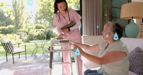 Caregiver assisting senior asian woman using walker indoors near sunlit garden patio doors