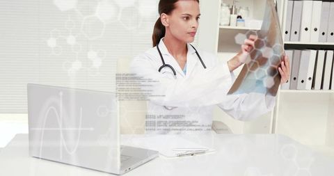 Female physician examining chest x-ray at clinic desk with laptop and stethoscope