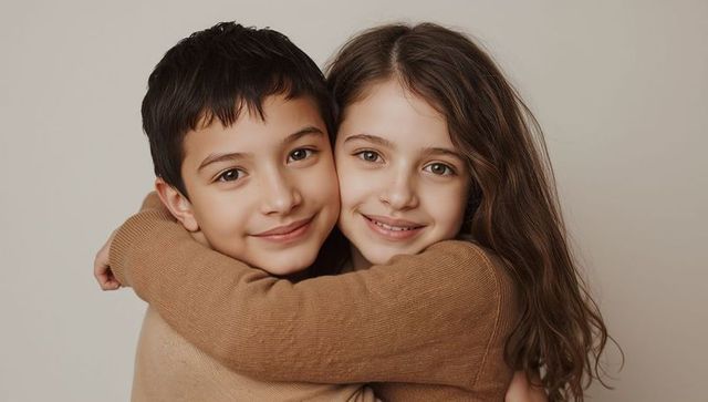 Siblings hugging and smiling closeup wearing brown knit sweaters on beige background