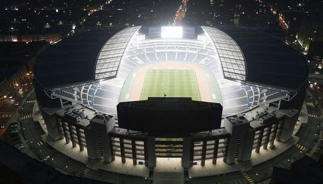 Aerial stadium illuminating urban nightscape, lit grass pitch and red running track