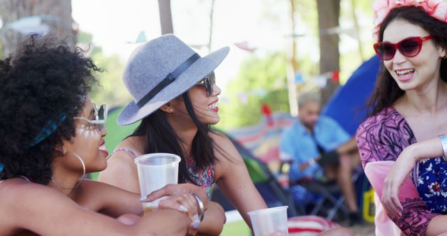 A diverse group of young women are enjoying a lively conversation at an outdoor event, with copy space. Their joyful expressions and summer attire suggest a relaxed and friendly atmosphere.