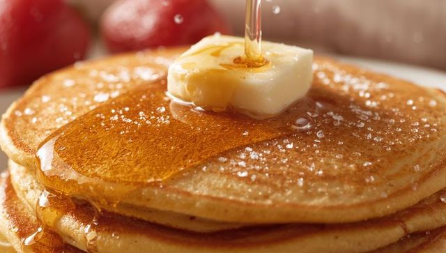 Drizzling maple syrup over buttered pancake stack with sparkling sugar crystals