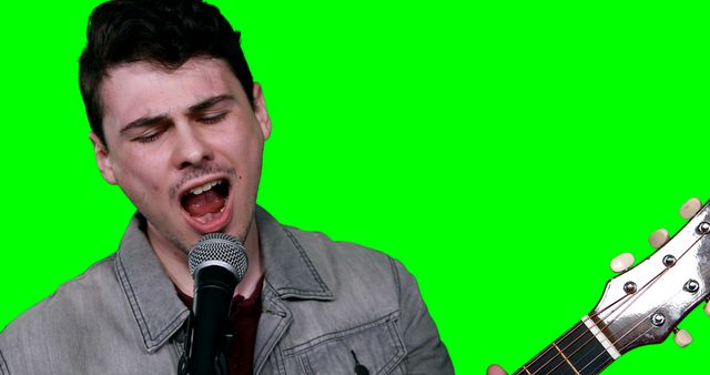 Male musician singing while playing guitar against green background