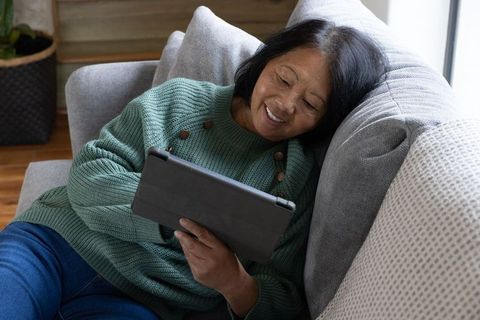 Smiling Senior Asian Woman Relaxing on Couch with Tablet