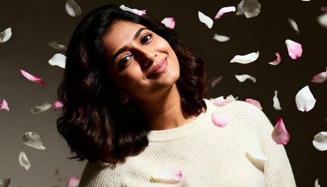 Smiling indian woman in cream sweater surrounded by falling pink rose petals
