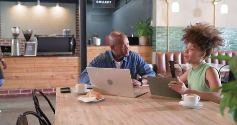 African american professionals collaborating on laptop and tablet in modern cafe workspace