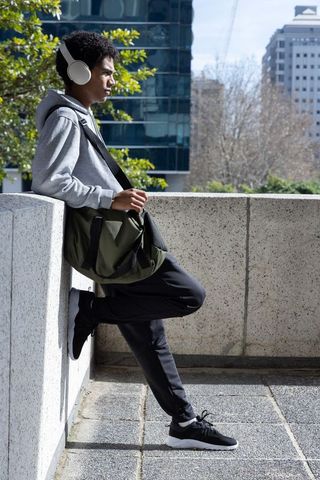 African american teen leaning on terrace parapet listening to headphones in urban cityscape