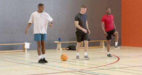 Three men stretching and warming up on indoor basketball court before practice