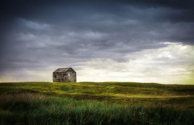 An isolated stone cabin stands alone on a vast, grassy prairie under a stormy sky. This calming natural scene is ideal for concepts of solitude, peace, and rural life. Perfect for backgrounds, environmental themes, and nature-focused content.