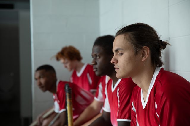 Side view of a multi-ethnic group of teenage male field hockey players, preparing before a game, sitting in the changing room and focusing. Sport game competition.
