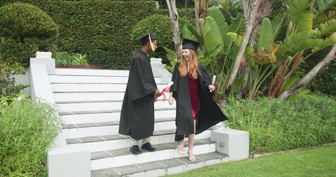 Graduates Celebrating on Garden Steps Wearing Caps and Gowns Holding Diplomas Smiling
