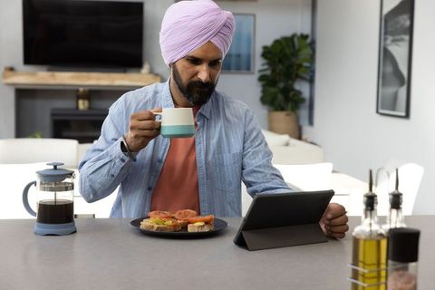 Man in Turban Enjoying Breakfast While Browsing Tablet at Kitchen Island