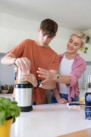 Woman guiding teen blending green smoothie on modern kitchen island healthy mentorship
